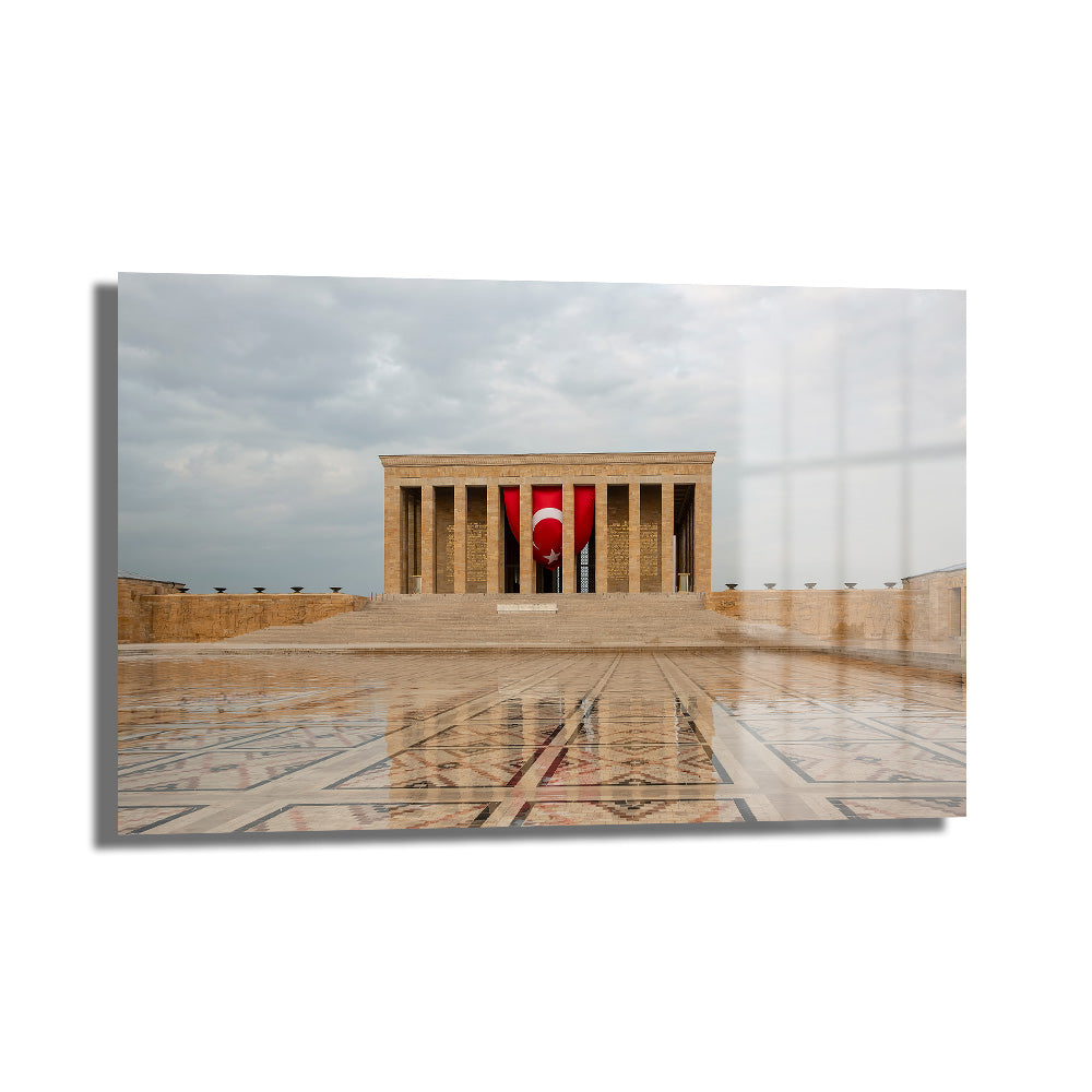Anıtkabir'in Görkemli Yansıması: Türk Bayraklı Cam Tablo, bulutlu havada ıslak zemine yansıyan Anıtkabir mimarisi ve dalgalanan Türk bayrağını betimler.
