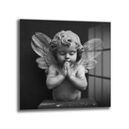 Siyah beyaz tonlarda, dua eden bir cherub (melek çocuk) heykelinin yakından çekilmiş fotoğrafı. Cherub'un gözleri kapalı, elleri göğsünde birleşmiş ve yüzünde huzurlu bir ifade var. Arkası karanlık, sağ tarafta pencere benzeri ışık yansımaları görülüyor. Heykelin dokusu ve detayları belirgin.
