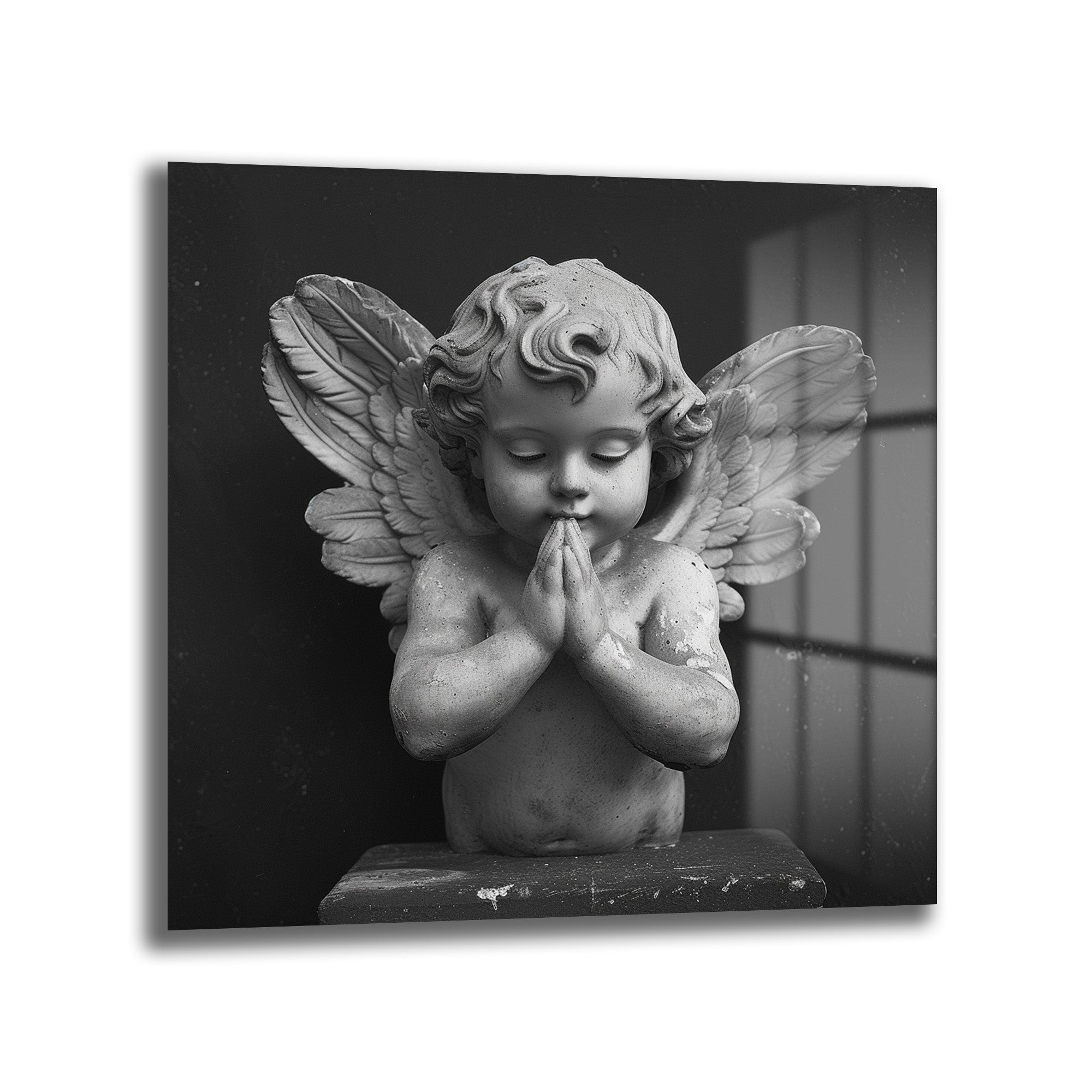 Siyah beyaz tonlarda, dua eden bir cherub (melek çocuk) heykelinin yakından çekilmiş fotoğrafı. Cherub'un gözleri kapalı, elleri göğsünde birleşmiş ve yüzünde huzurlu bir ifade var. Arkası karanlık, sağ tarafta pencere benzeri ışık yansımaları görülüyor. Heykelin dokusu ve detayları belirgin.