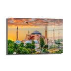 Ayasofya'da Gün Batımı: İstanbul'un Görkemli Manzarası Cam Tablo, turuncu ve mor tonlarında gün batımı gökyüzünün altında Ayasofya'nın minare ve kubbelerini gösteren, uçuşan martılarla süslenmiş büyüleyici bir İstanbul manzarası.