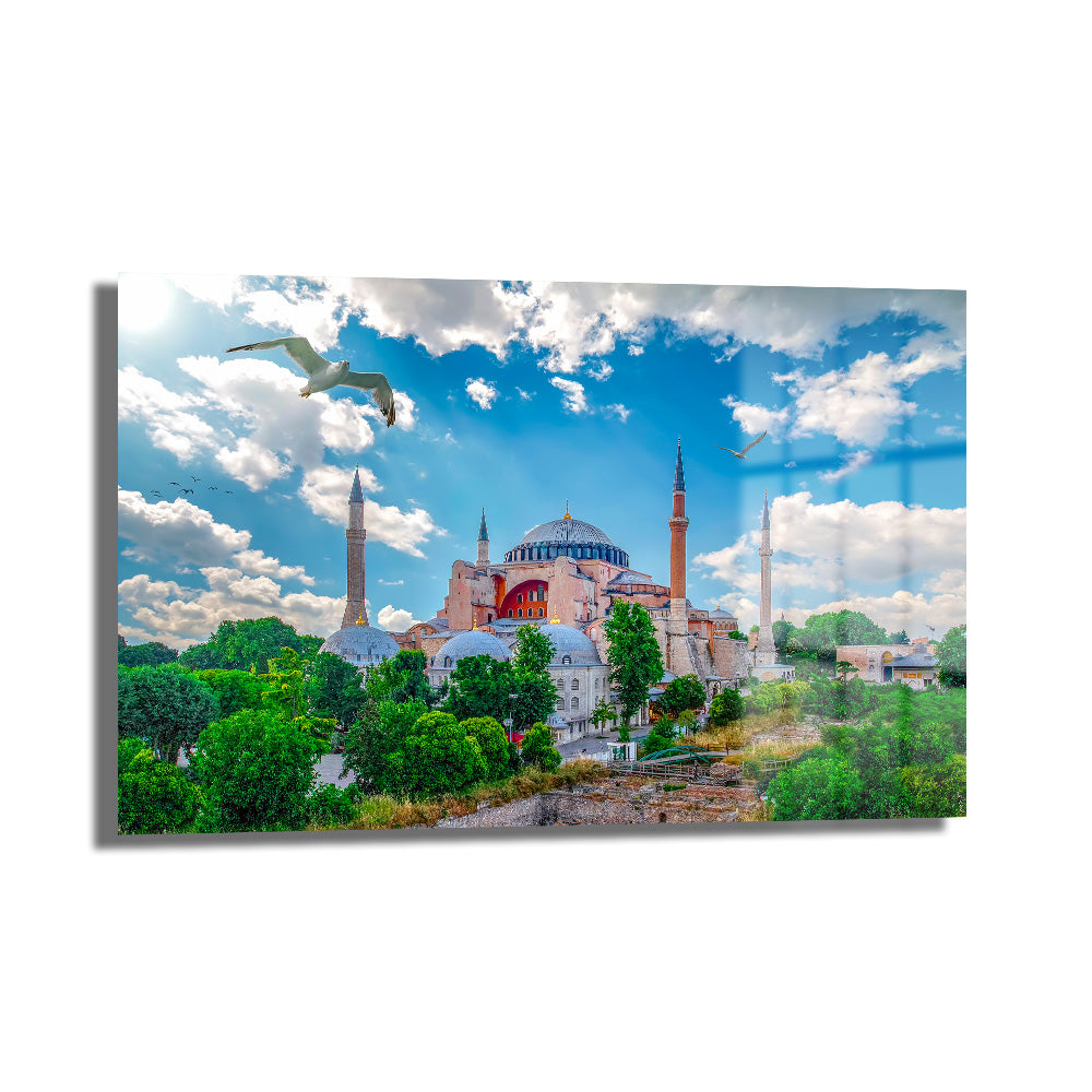 Ayasofya'nın Işıltısı: İstanbul Manzaralı Dekoratif Cam Tablo, masmavi gökyüzü, süzülen martılar ve yeşil ağaçlar eşliğinde Ayasofya'nın görkemli silüetini gösteren modern ve şık bir duvar dekoru.