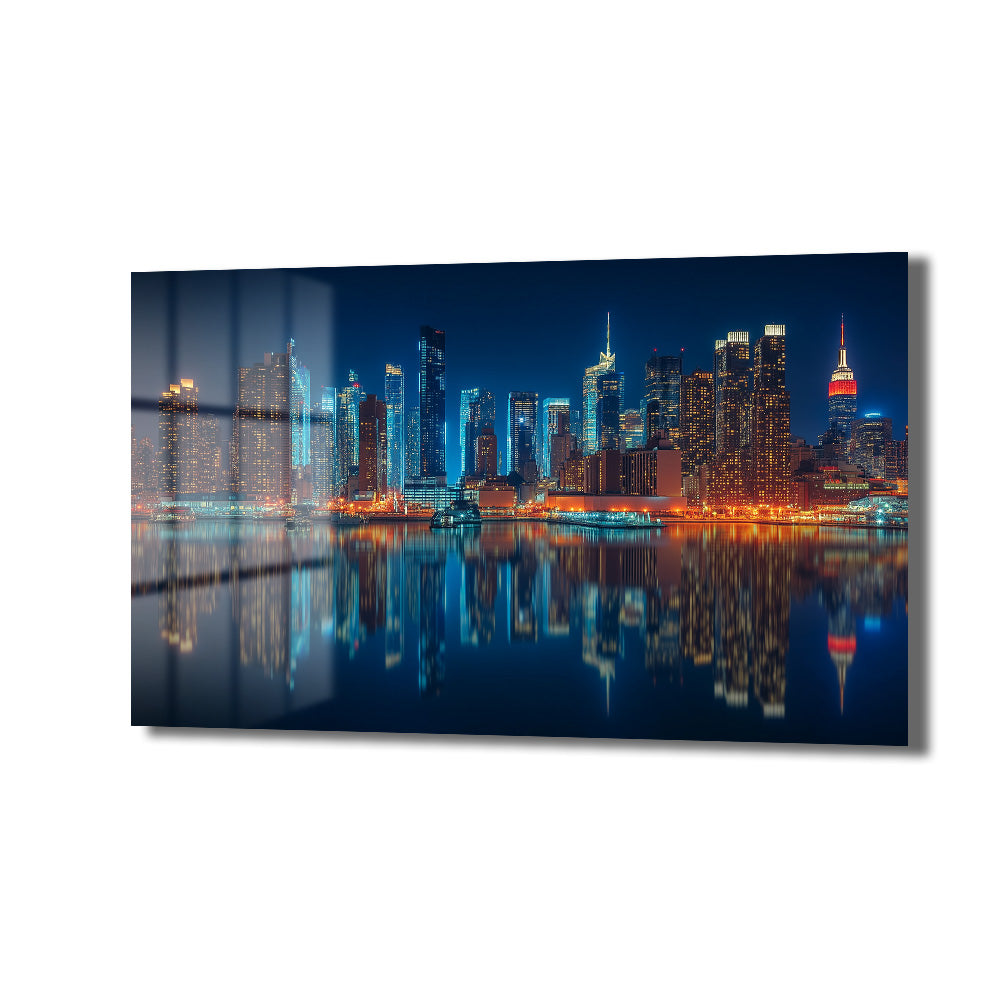 New York şehir silüetinin gece ışıklarıyla parladığı, suya yansıyan büyüleyici görüntüsünü içeren temperli cam tablo, modern salon ve ofis dekorasyonu için şık bir duvar sanatı.