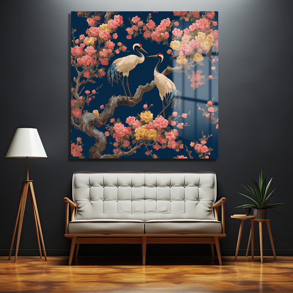 Koyu lacivert duvarda asılı, lacivert zemin üzerine pembe ve sarı çiçeklerle bezeli bir ağaç dalında duran iki zarif turnayı gösteren büyük, parlak cam tablo. Turnaların beyaz tüyleri, kırmızı başları ve mavi kanat detayları dikkat çekiyor.