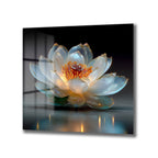 Karanlık ve yansıtıcı bir zeminde, ışıkla parlayan, şeffaf ve altın detaylı lotus çiçeği motifli cam tablo. Çiçeğin merkezi kırmızı ve turuncu tonlarda, yaprakları beyaz ve açık mavi renklerde.
