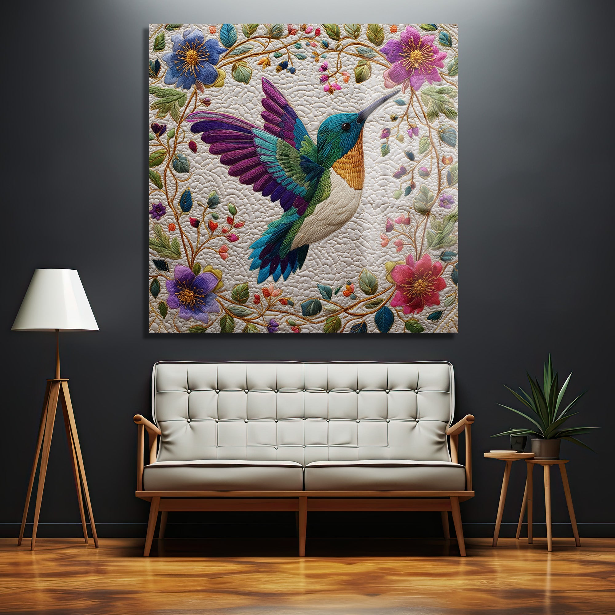 Modern ve minimalist bir salonda, koyu gri duvarda asılı, canlı renklerde işlenmiş kolibri ve etrafındaki çiçek motifleriyle bezenmiş büyük bir cam tablo. Tablonun altında beyaz döşemeli ahşap ayaklı bir kanepe, solunda ahşap lambader ve sağında yeşil bir bitki yer almaktadır.