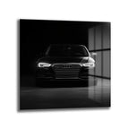 Karanlık bir ortamda, parlak farları açık, önden çekilmiş siyah renkli modern Audi otomobilin cam tablo görünümü.