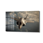 Gri renkli modern bir F-35 hayalet savaş uçağı, bulutlu gökyüzünde dağların üzerinden uçarken önden çekilmiş dinamik bir görünüm. Kanatlar ve gövde detayları belirgin.