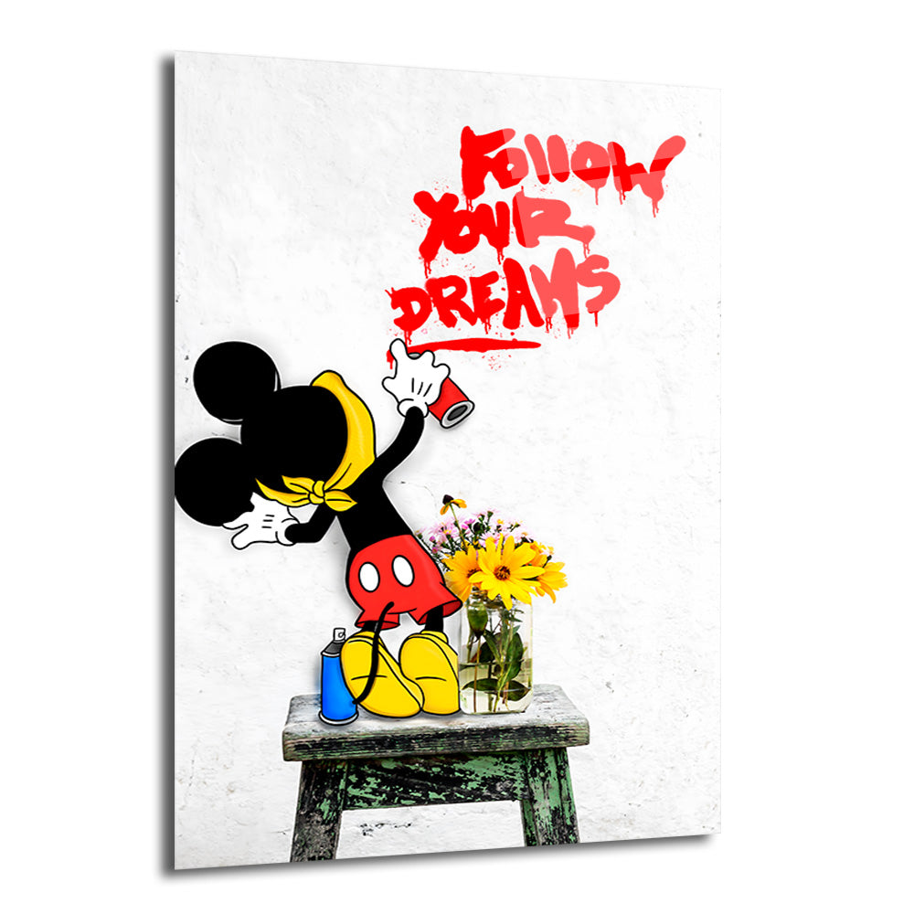 Beyaz bir duvarda Banksy tarzı figürü, kırmızı sprey boyayla 'Follow Your Dreams' yazısını yazarken, yanında bir iskemle üzerinde sarı çiçekler ve mavi bir sprey kutusu bulunuyor.
