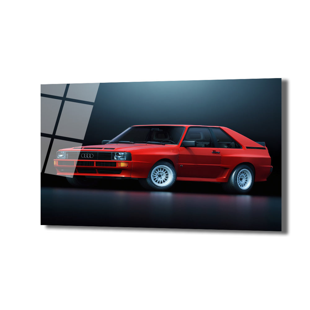 Koyu arka plan üzerinde parlak kırmızı renkte, klasik bir Audi Quattro spor arabanın yan profilden çekilmiş fotoğrafı. Arabanın beyaz jantları ve farları dikkat çekiyor.