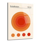 Kremsi beyaz bir arka plan üzerinde, merkezde turuncu ve kırmızı tonlarında iç içe geçen dairelerden oluşan, Bauhaus 1919 yazılı, modern ve soyut bir cam tablo. Alt kısımda dört küçük renk örneği dairesi bulunmaktadır.