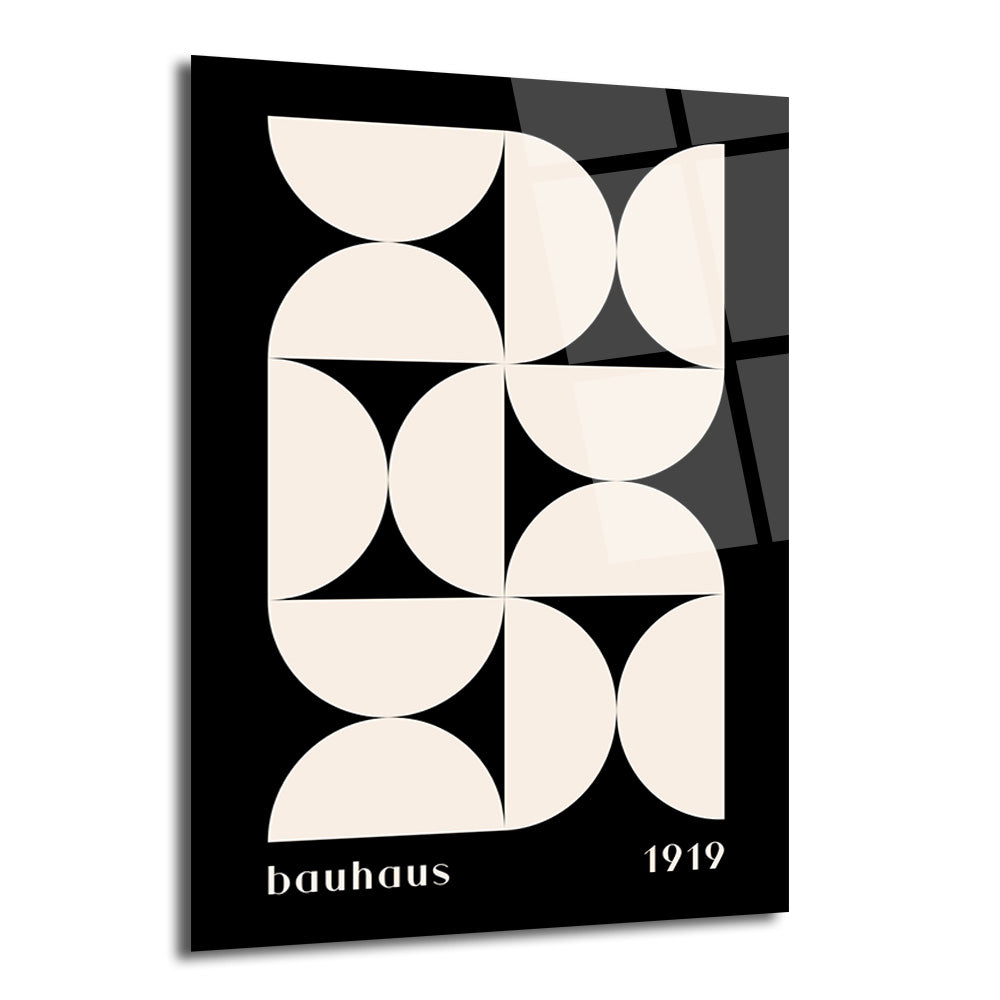 Siyah zemin üzerinde bej renkli yarım dairelerin simetrik ve geometrik desen oluşturduğu, alt kısmında 'bauhaus' ve '1919' yazan minimalist bir cam tablo.