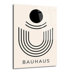 Açık bej bir zeminde siyah bir daire ve altında eşit aralıklarla sıralanmış, U şeklinde geometrik çizgilerle oluşturulmuş minimalist bir tasarımın yer aldığı, altında 'BAUHAUS' yazan parlak cam tablo.