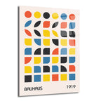 Krem rengi zeminde kırmızı, sarı, siyah ve mavi renklerde Bauhaus tarzı geometrik şekillerden (tam daireler, yarım daireler, çeyrek daireler ve yaprak benzeri formlar) oluşan, 'BAUHAUS' ve '1919' yazılarının yer aldığı parlak bir cam tablo.