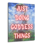 Monet tarzı bir resmin üzerine pembe, parlayan harflerle "JUST DOING GODDESS THINGS" yazısının eklendiği, elinde şemsiye tutan bir kadını ve arkasında mavi gökyüzü ile yeşil çimenleri gösteren modern cam tablo.