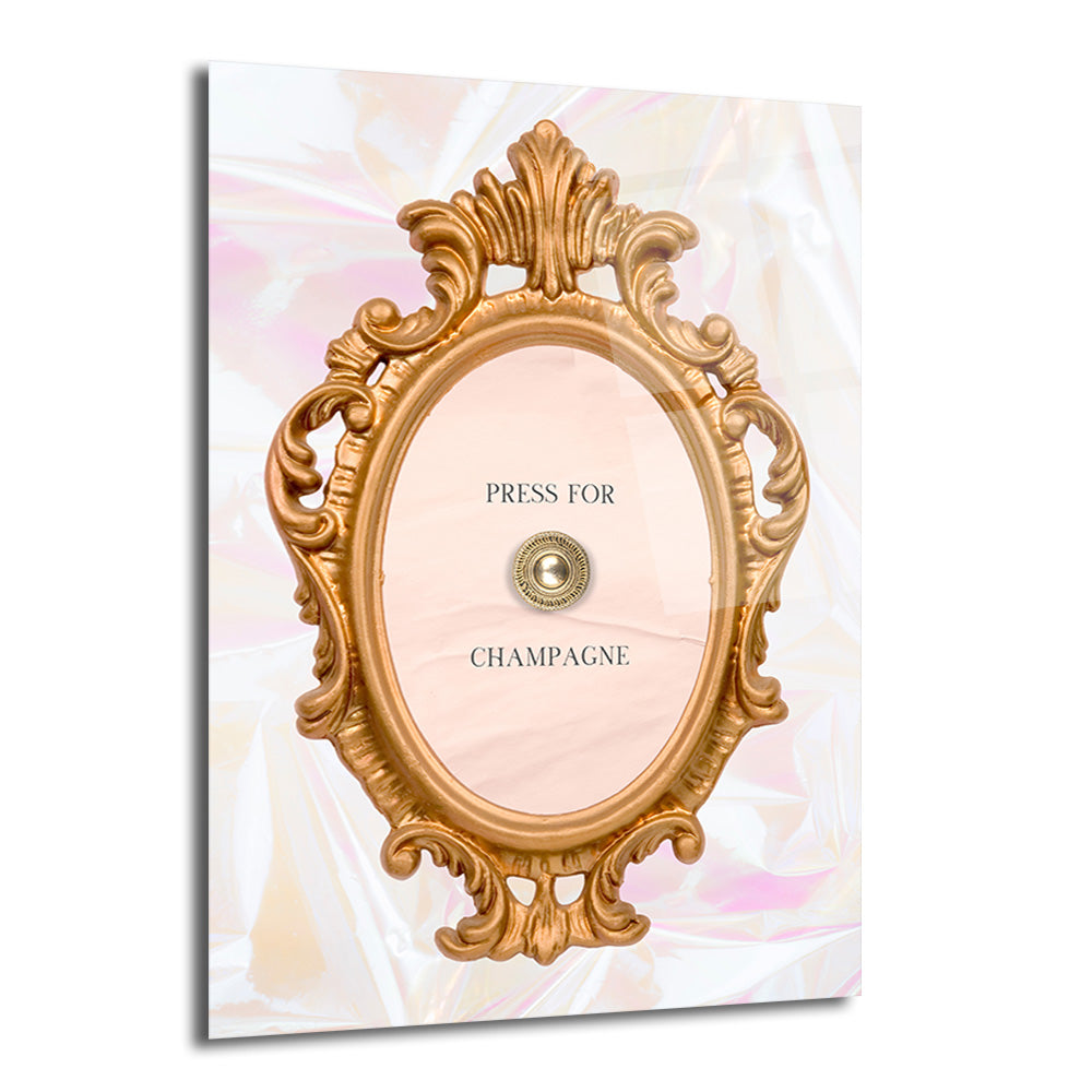Altın renkli, oymalı, oval bir çerçeve içerisinde 'PRESS FOR' ve 'CHAMPAGNE' yazıları ile ortasında dekoratif bir zil düğmesi bulunan, sedefli pembe ve beyaz tonlarında parıltılı bir arka plana sahip modern cam tablo.