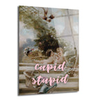 Klasik bahçe sahnesinde iki çerubun yer aldığı, üzerine pembe renkte 'cupid stupid' yazısı eklenmiş modern ve esprili cam tablo.