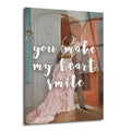 Pembe elbiseli bir kadının ve takım elbiseli bir erkeğin kapı eşiğinde sarıldığı, üzerinde 'You Make My Heart Smile' yazısı bulunan romantik bir cam tablo.