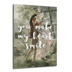 Yeşil ve beyaz çiçekli bir bahçede dans eden klasik giyimli romantik bir çiftin resmedildiği, üzerinde 'You Make My Heart Smile' yazılı Glazella cam tablo.