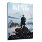Sisli dağ manzarasına bakan, zirvede duran bir adamın arkasından çekilmiş, gökyüzünde parlayan 'KING' yazısı ve sanatsal kar taneleri içeren, Caspar David Friedrich esintili modern bir cam tablo.