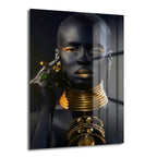 Altın Işıltılı Asalet: Modern Afrika Kraliçesi Cam Tablo, altın rengi takılar ve makyajla vurgulanmış asil bir Afrika kraliçesi portresini sergileyen, temperli cam üzerine UV baskı ile üretilmiş modern bir duvar dekorasyonudur.